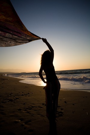 Young woman standing on rock in sea and looking to a sunの写真素材