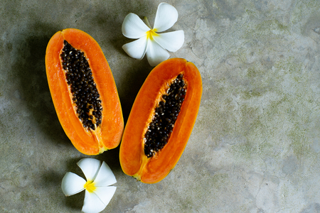 Papaya fruit on grey background. Slices of sweet papaya on grey background with white flowersの写真素材