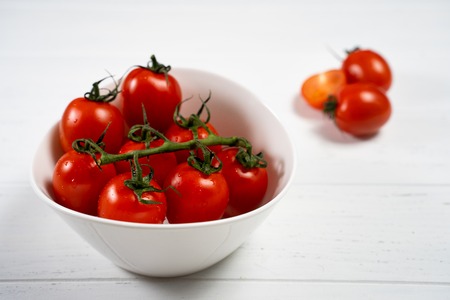 Fresh cherry tomatoes in a plate on a white wood background.の写真素材