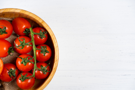 Fresh cherry tomatoes in a wooden plate on a white wood background.の写真素材