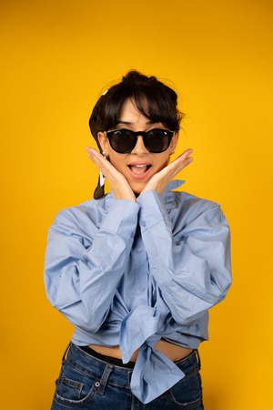 Young girl with in sunglasses posing for a photo on yellow background.の写真素材