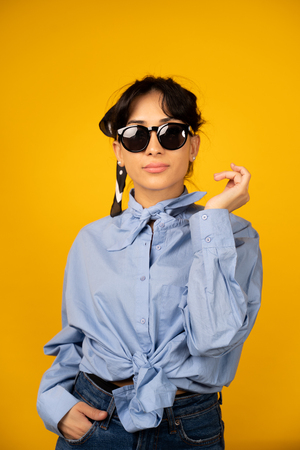 Young girl with in sunglasses posing for a photo on yellow background.の写真素材