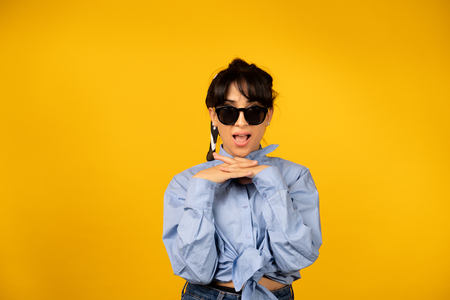 Young girl with in sunglasses posing for a photo on yellow background.の写真素材