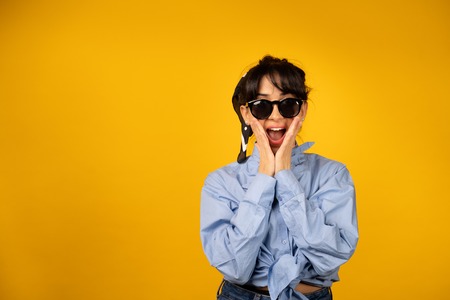 Young girl with in sunglasses posing for a photo on yellow background.の写真素材