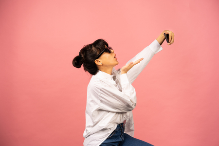 Young girl in sunglasses making selfie on a pink background.の写真素材