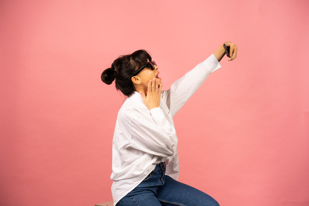 Young girl in sunglasses making selfie on a pink background.の写真素材