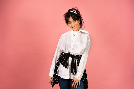 Young beautiful girl in a white shirt posing for a photo on a pink background.の写真素材