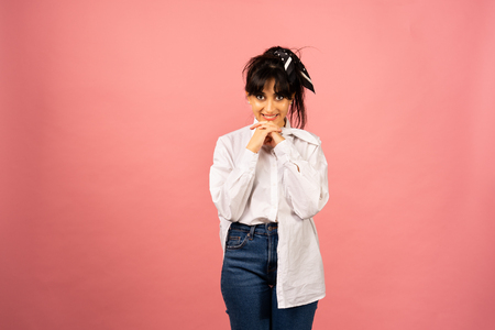 Young beautiful girl in a white shirt posing for a photo on a pink background.の写真素材