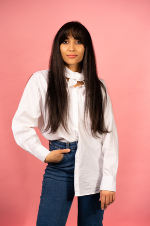Young beautiful girl in a white shirt posing for a photo on a pink background.の写真素材