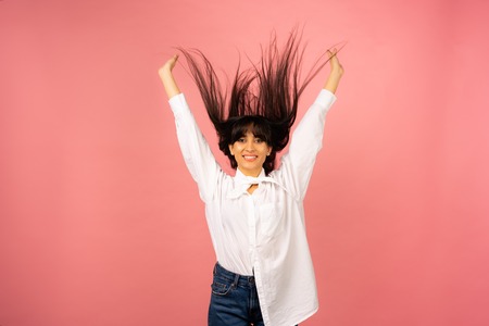 Young beautiful girl in a white shirt posing for a photo on a pink background.の写真素材