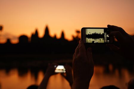 A man takes a photo of sunrise and the temple of Ankor Wat on the phoneの写真素材