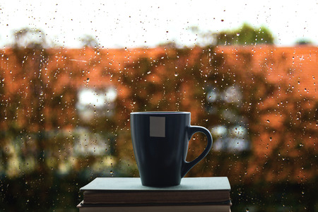 Books and coffee on window, rain drops on glass in background