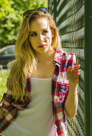 Beautiful trendy hipster girl standing next to fence in parkの写真素材