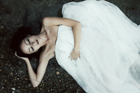 Woman lying on the shore in white dress dark mystery sceneの写真素材