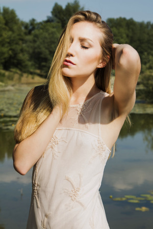 Beautiful blonde girl in white dress outdoor emotive expression eyes closedの写真素材