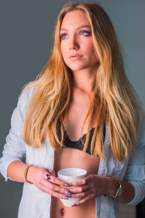 Young blonder sexy woman in underwear holding cup of coffee in the morningの写真素材