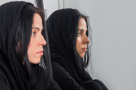Portrait of serious young woman with covered hair, reflection in mirrorの写真素材