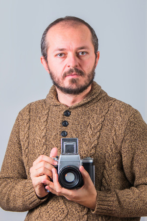 Man with beard in sweater holding old analogue medium format cameraの写真素材