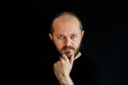 Serious man on black background in low key, holding arm on chin, thoughtfulの写真素材