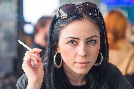 Young girl sitting in cafe, holding cigarette and looking to cameraの写真素材