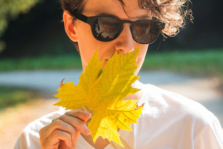 Portrait of a beautiful young woman smelling colorful leaves in autumnの写真素材