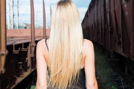 Beautiful blonde girl walking on rail tracks, romantic look, from backの写真素材