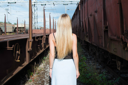 Beautiful blonde girl walking on rail tracks, romantic look, from backの写真素材