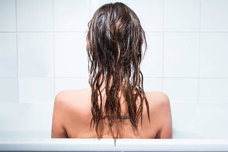 Young girl sitting in bathtub, alone and depressed, back, wet hairの写真素材