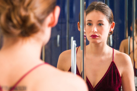 Portrait of beautiful young woman in red dress with naked back, standing in front of the mirror, beauty fashion concept, blurred backgroundの写真素材