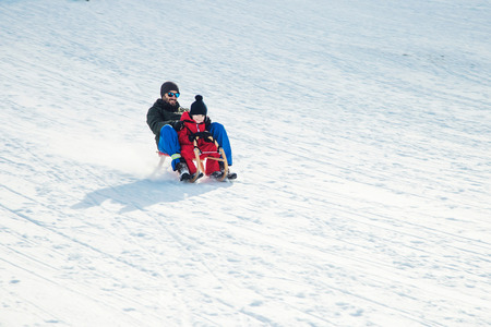 Happy father and his son enjoying sledding ride. Happy family with sled in winter having fun together. Fast ride. Family driving sled under winter snow. Winter holidays.の写真素材