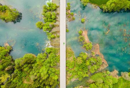 Road trip in wild nature landscape - car crossing road bridge over Mreznica river in Croatia, overhead shot of countryside landscape, waterfalls and trees in springの写真素材