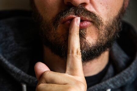 Don't speak, be quiet - close up portrait of bearded man on the door saying shh. Finger on lips. Head and shoulders, no eyes. Danger. Violence concept.の写真素材
