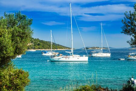 Scenic view of Kosirina beach bay on Murter island in Croatia, anchored sailing boats and yachts on blue sea, view through the pinesの写真素材