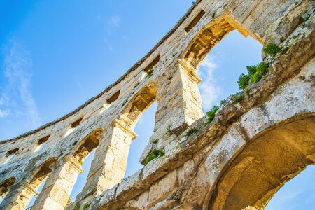 Ancient heritage in Pula, Istria, Croatia. Arches of monumental Roman arena. Detail of historic amphitheater, wide angle view of walls on blue sky background.の写真素材