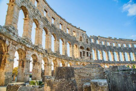 Ancient heritage in Pula, Istria, Croatia. Arches of monumental Roman arena. Detail of historic amphitheater, wide angle view of walls on blue sky background.の写真素材