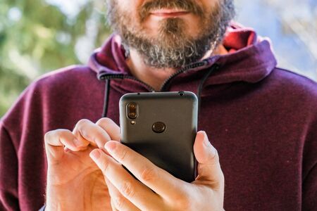 Man at park using smart phone, reading or typing a message on cellphone while, hands detailの写真素材