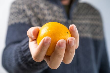 Man in the sweater giving the orange, hands detail, blurred background, shallow debt of field