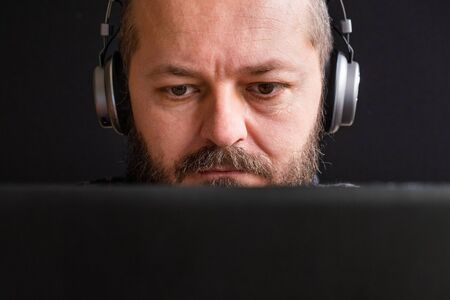 Close up portrait of caucasian adult man in vintage sweater sitting behind the laptop and typing,...