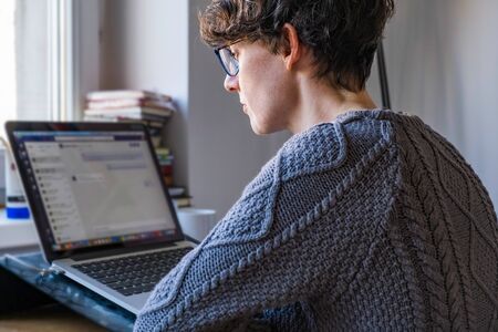 Young caucasian entrepreneur woman in sweater sitting and working online from home on computer...