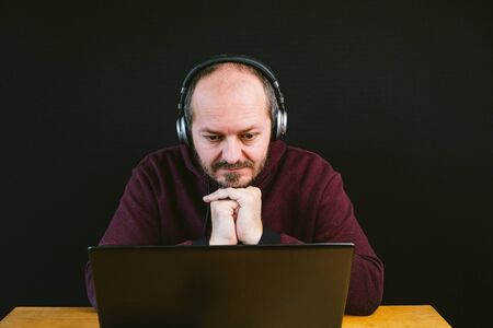 Man in hoodie and headphones on head sitting behind the laptop, confused, unsuccessful, black...