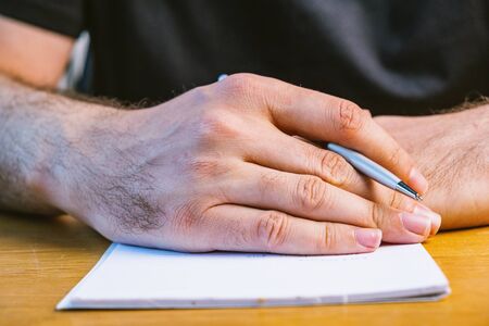 Detail of hand of businessman holding pen over notebook on office deskの写真素材