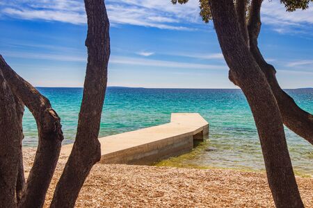 Croatia, island of Pag, beautiful beach under pine trees, turquoise water of Adriatic Sea and long pier on sunny summer day. Famous tourist destination.の写真素材