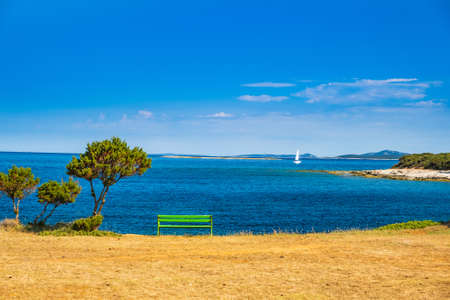 Beautiful Adriatic shore in Croatia, Dugi Otok island. Bench and sailing boat on sea in bay on Veli Rat.の写真素材