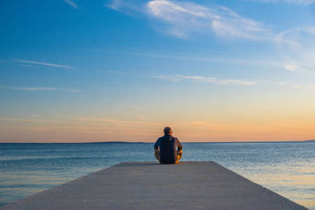 Man sitting on the edge of dock and meditating. Sea horizon at sunset, island od Pag, Adriatic sea, Croatia.の写真素材