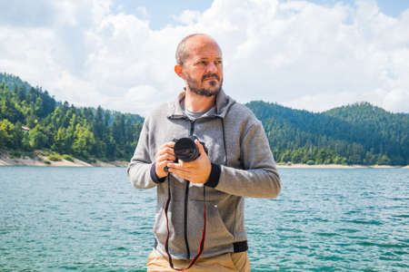 Photographer man in hoodie walking around lake with DSLR camera and shooting nature, half body portrait, landscape photography conceptの写真素材