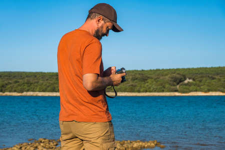 Photographer man in t-shirt and cargo pants walking around sea shore with camera and shooting...