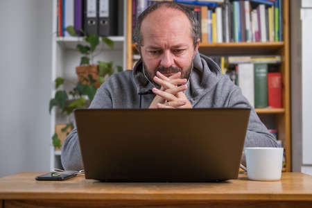 Man working online from home office on computer laptop behind vintage desk, with earphones, listening online meetingの写真素材