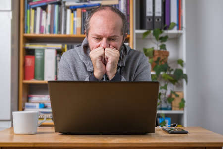Man working online from home office on computer laptop behind vintage desk, with earphones, listening online meetingの写真素材
