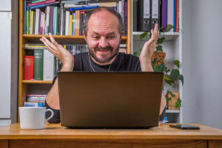 Man working online from home office on computer laptop behind vintage desk, with earphones, listening online meeting and drinking coffeeの写真素材