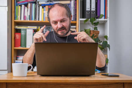 Man working online from home office on computer laptop behind vintage desk, with earphones, listening online meeting and drinking coffeeの写真素材